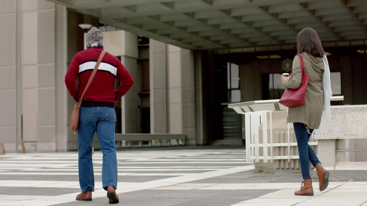 Diverse coworkers walking plaza toward entry as man entering and woman joining with bags and coffee