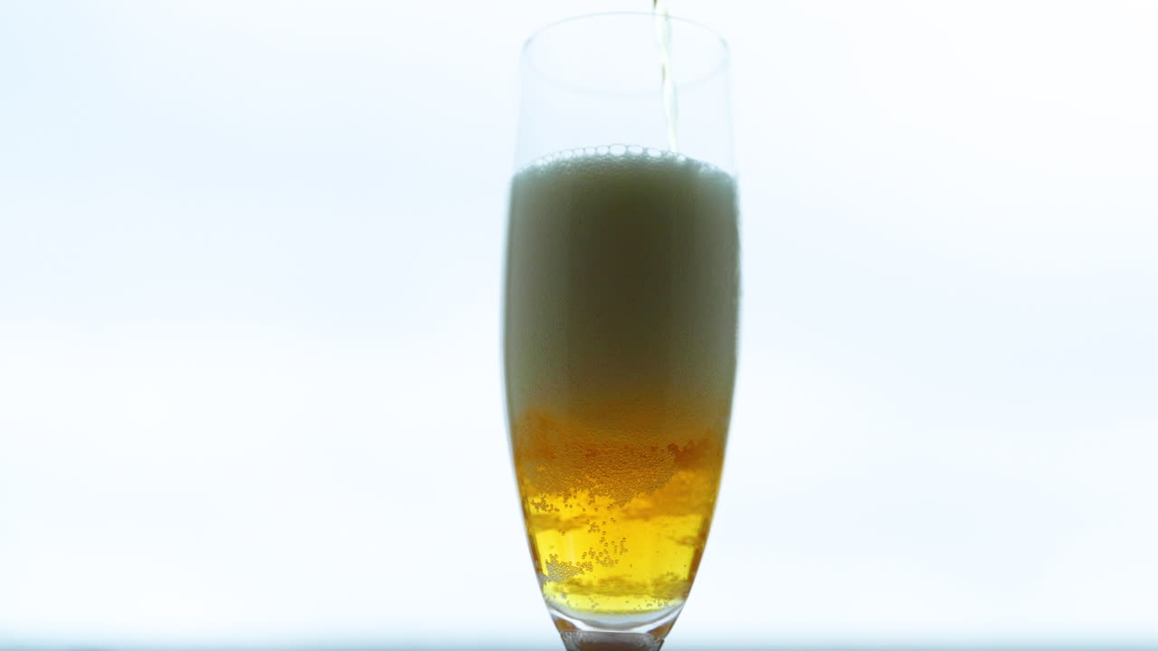 슬로우 모션 캡처에서 좁은 유리를 통해 움직이는 전구로 조밀하고 높은 거품이 형성되는 매체에서 유리를 채우는 맥주