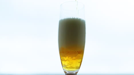 cerveza llenando un vaso de un medio donde se forma una espuma densa y alta con bulbos moviéndose a través de un vaso estrecho en captura de cámara lenta