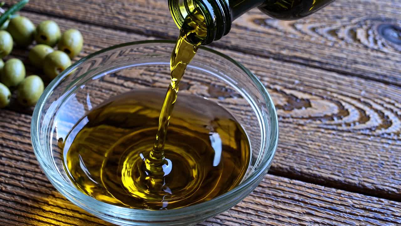 Close-up video shot of olive oil pouring into a glass bowl on rustic wooden table