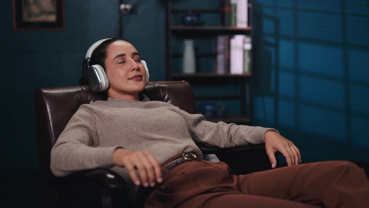 Mujer joven relajándose en un sillón de cuero mientras escucha música.