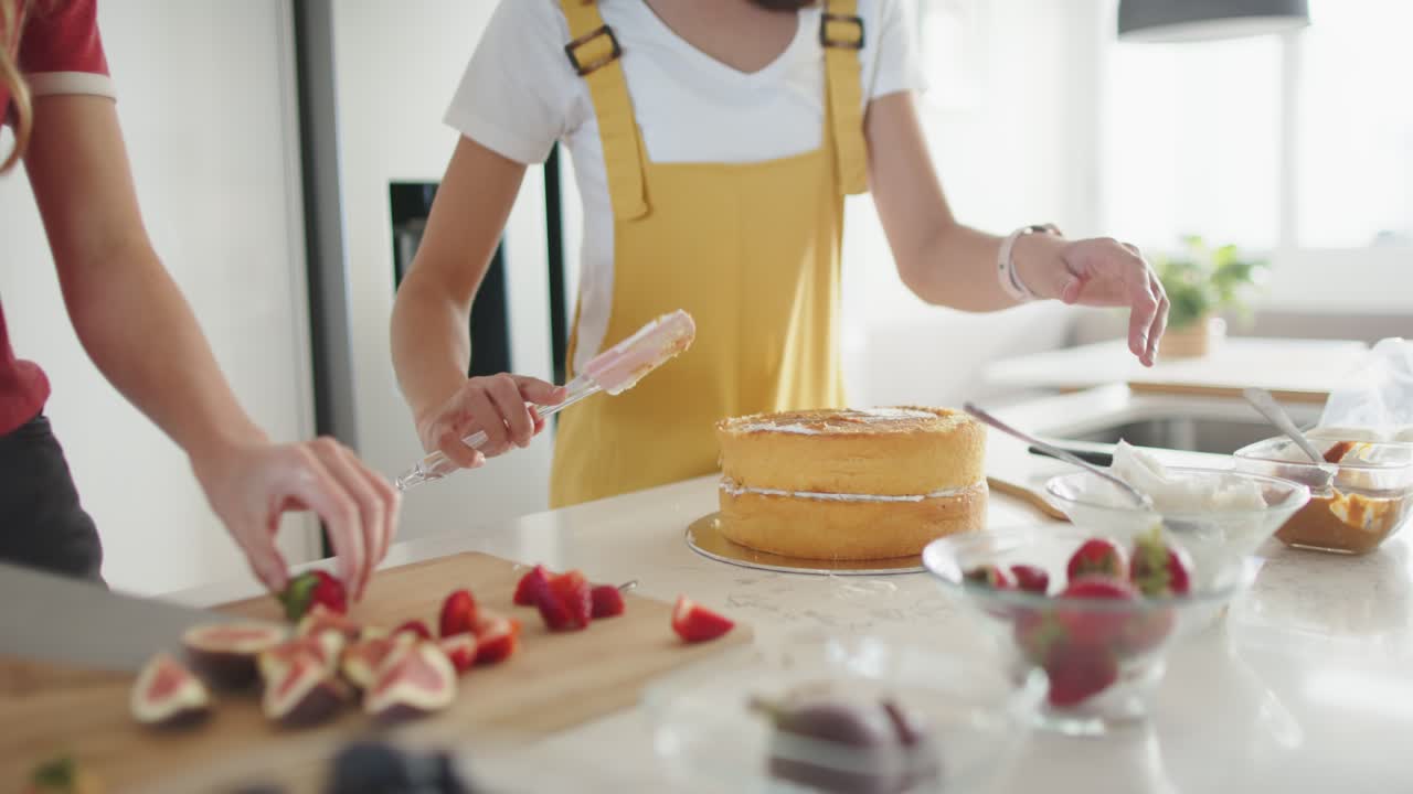 Unas amigas consultan una receta en el smartphone y cortan fruta para decorar una tarta en la isla de la cocina.