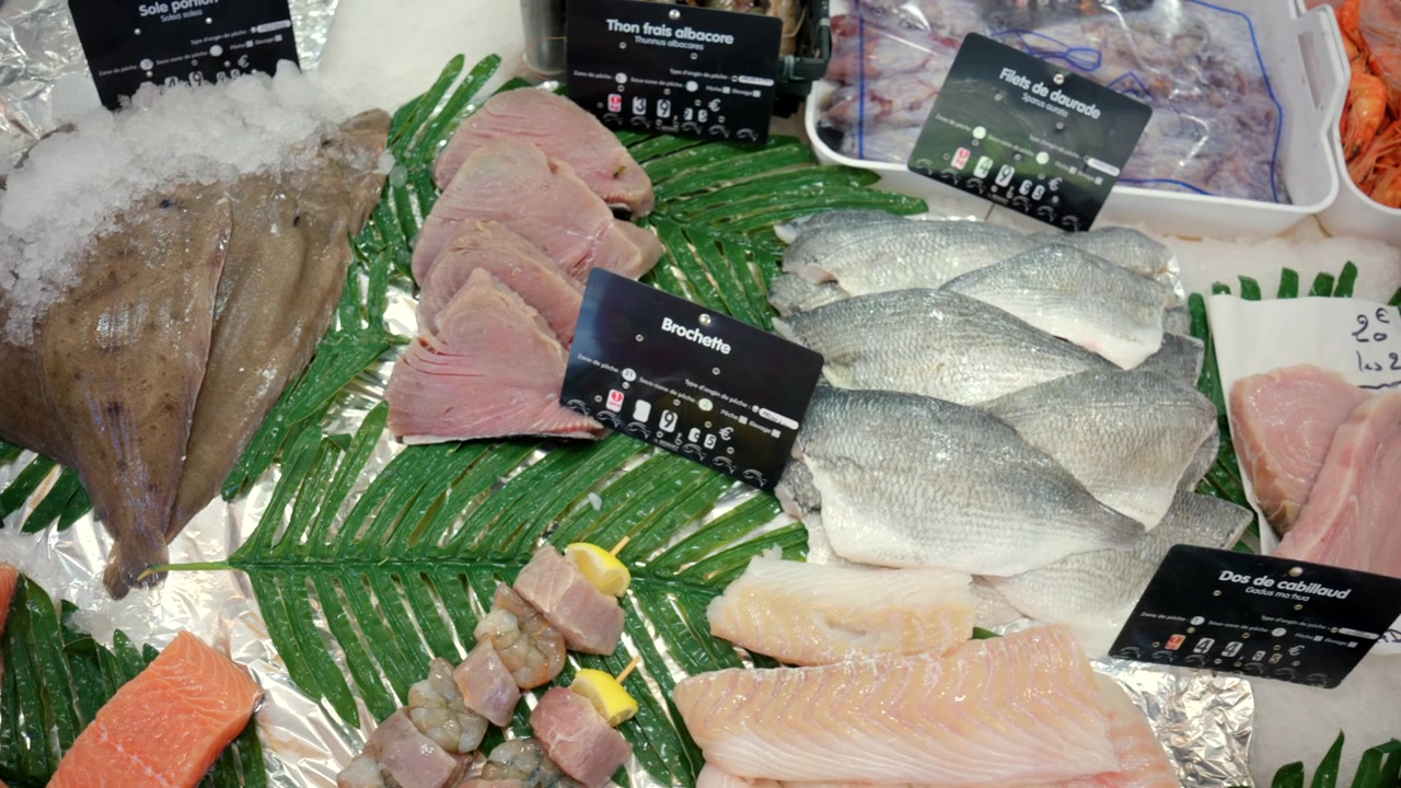 Displaying various raw seafood products including cod fillets and whole fish, arranged on ice at a market stall