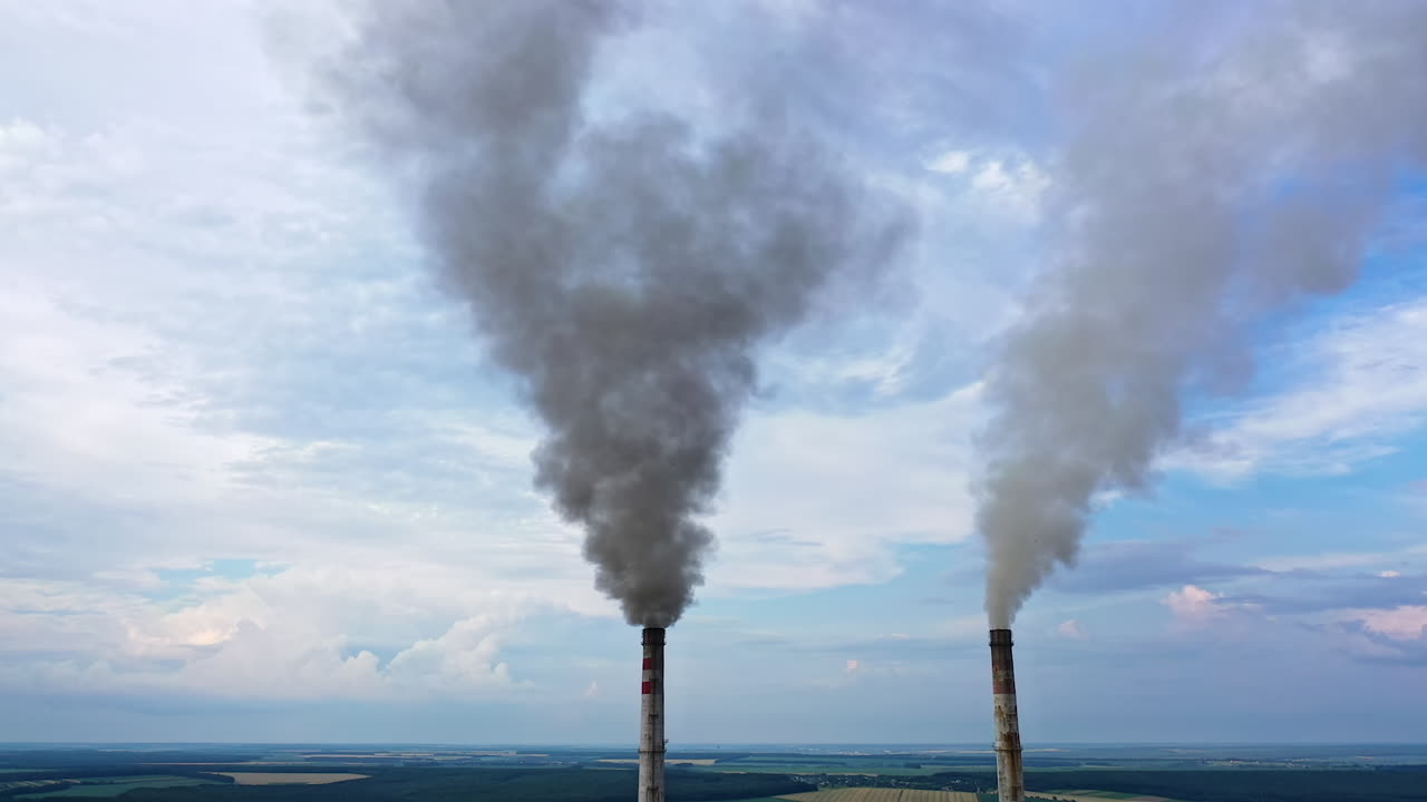 View from the drone at the old aged weathered tall industrial factory chimney with smoke over it. Cloudy sky background