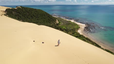 Man-walking-on-huge-sand-dune,-exploring-beautiful-view-of-tropical-coastal