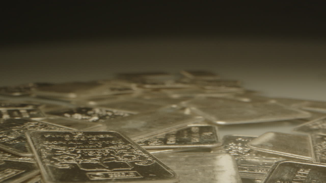Beautiful macro dolly out of many silver bars spread out on a white surface. The precious metal plates are cinematically lit while the camera moves over the shiny plates