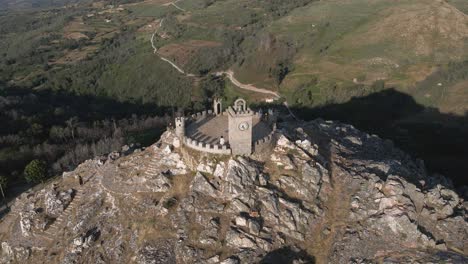 Tourist-stands-on-the-towers-of-the-Folgosinho-Castle-as-a-drone-circle-at-sunset