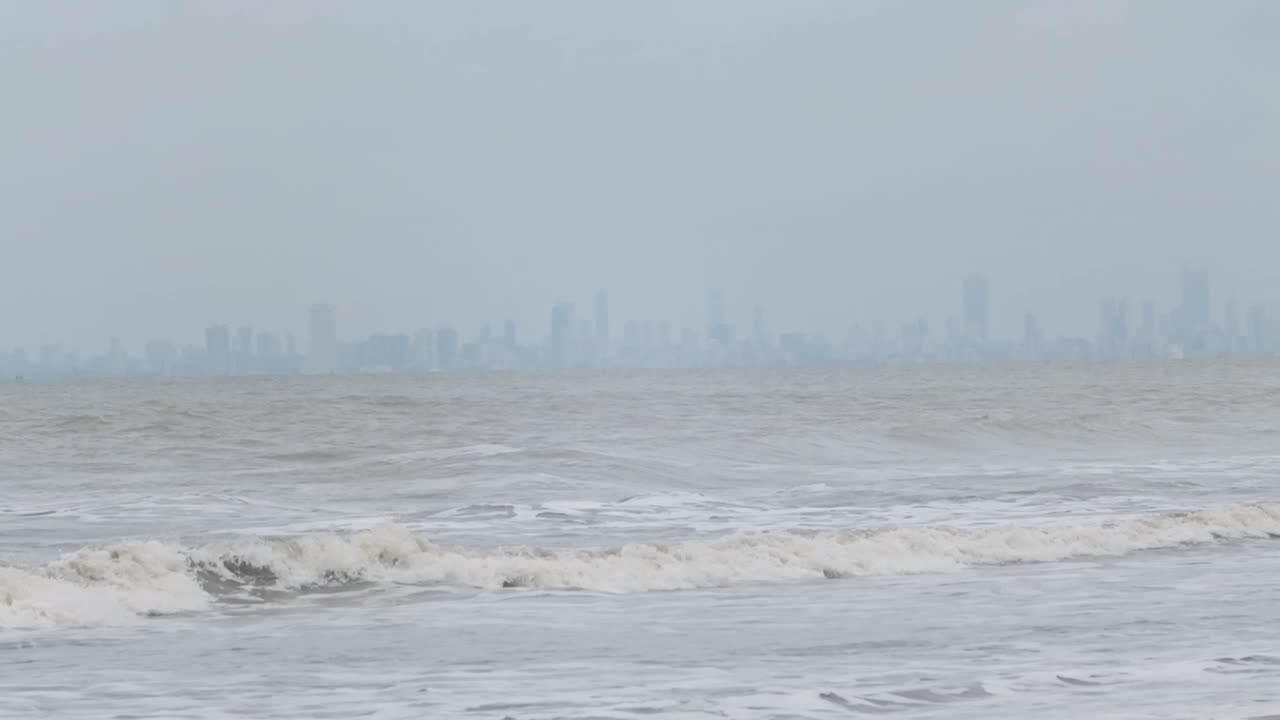 배경 슬로우 모션으로 대형 타워 시티가 있는 해변에 부서지는 파도