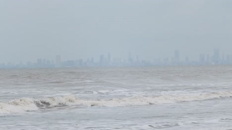 waves crashing on a beach with large tower city in the background slow motion