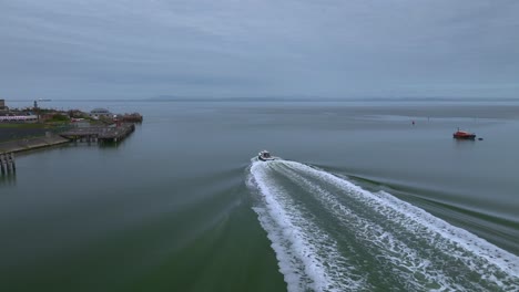 Following-boat-with-wide-wake-as-it-heads-out-towards-sea-from-calm-river