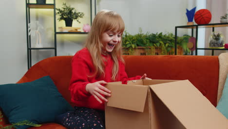 little child girl shopper unpacking cardboard box delivery parcel online shopping purchase at home