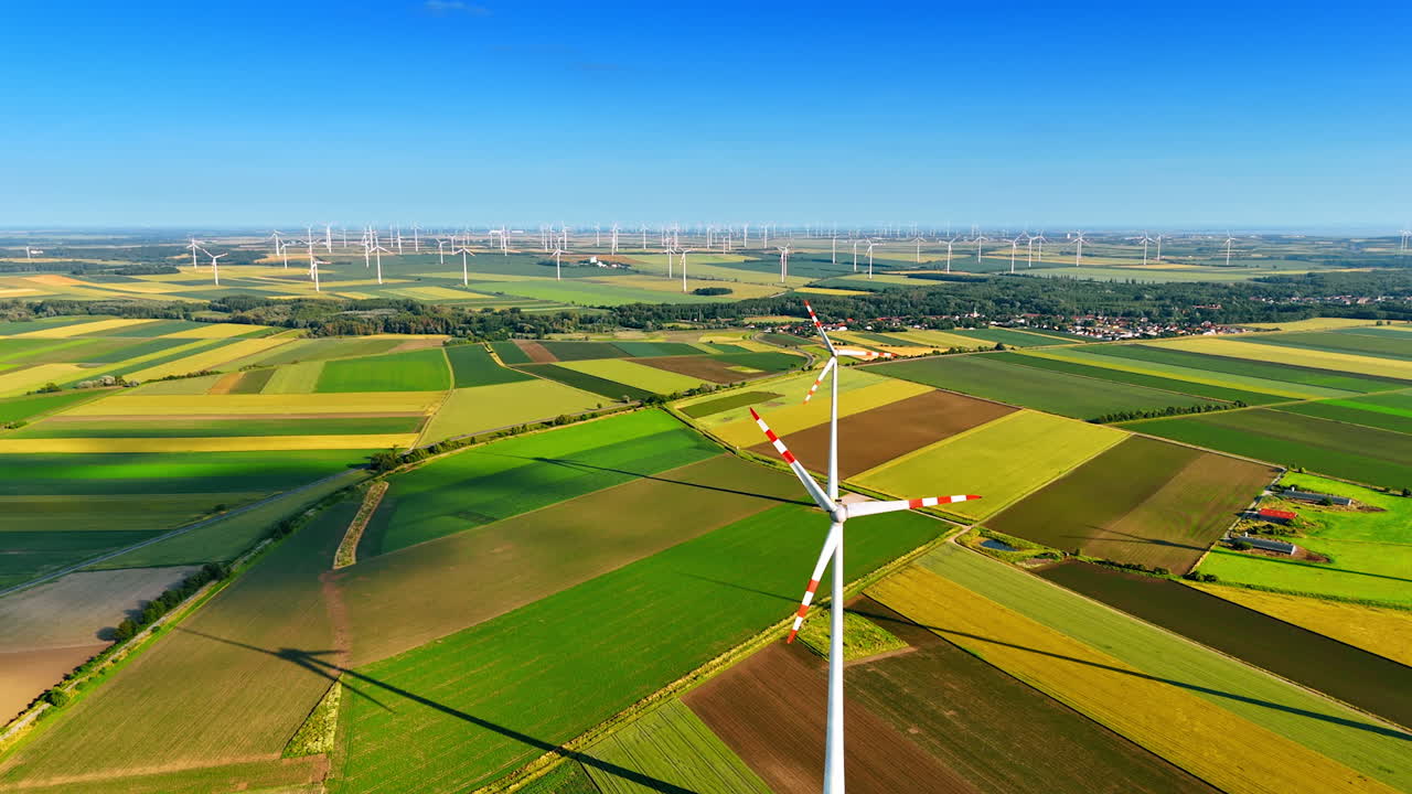 Turbines produce clean energy. Wind turbines rotate above lush fields, harnessing renewable energy in a vast rural landscape under a clear blue sky