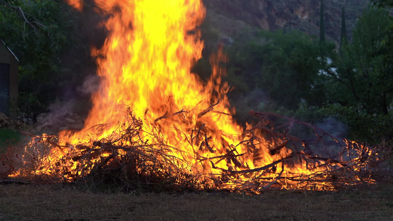 un fuego controlado quema una gran pila de escombros de madera en un claro del bosque, el humo se eleva contra un cielo despejado, evitando incendios forestales