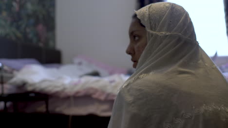 primer plano de una chica musulmana con un hiyab de color blanco rezando en su habitación