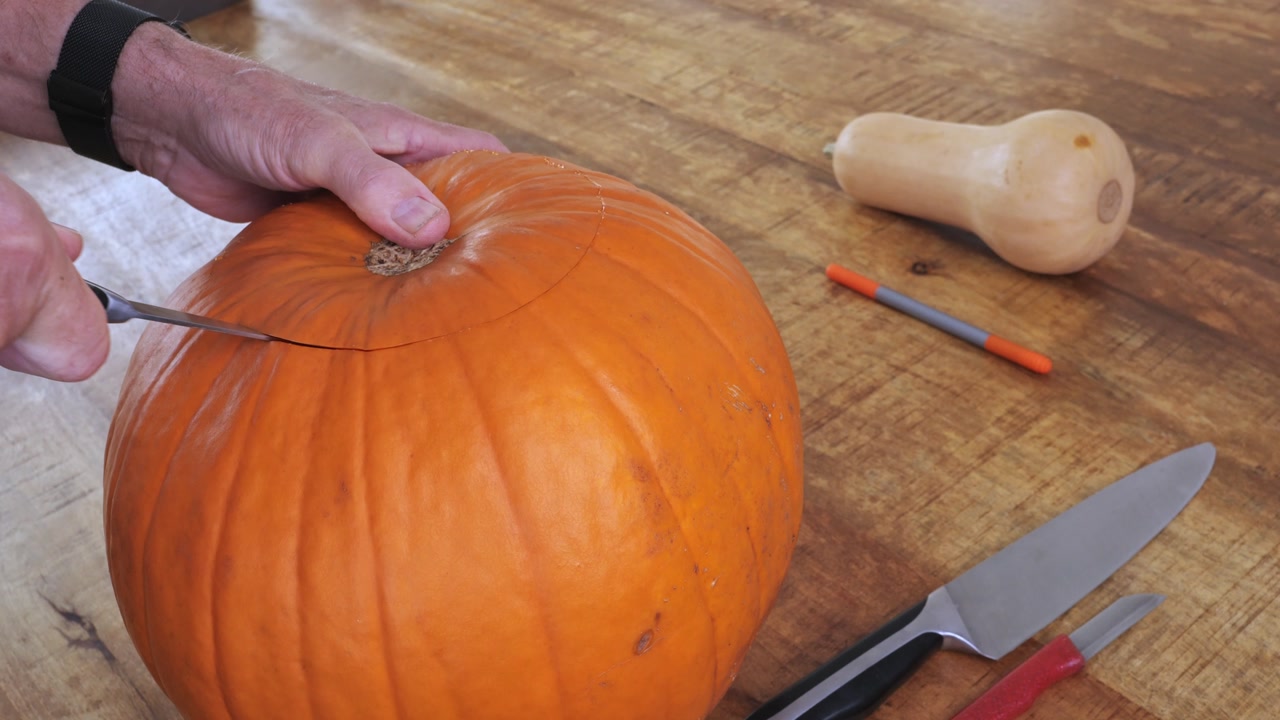 Closeup of hands cutting pumpkin to create Halloween jack-o’-lantern