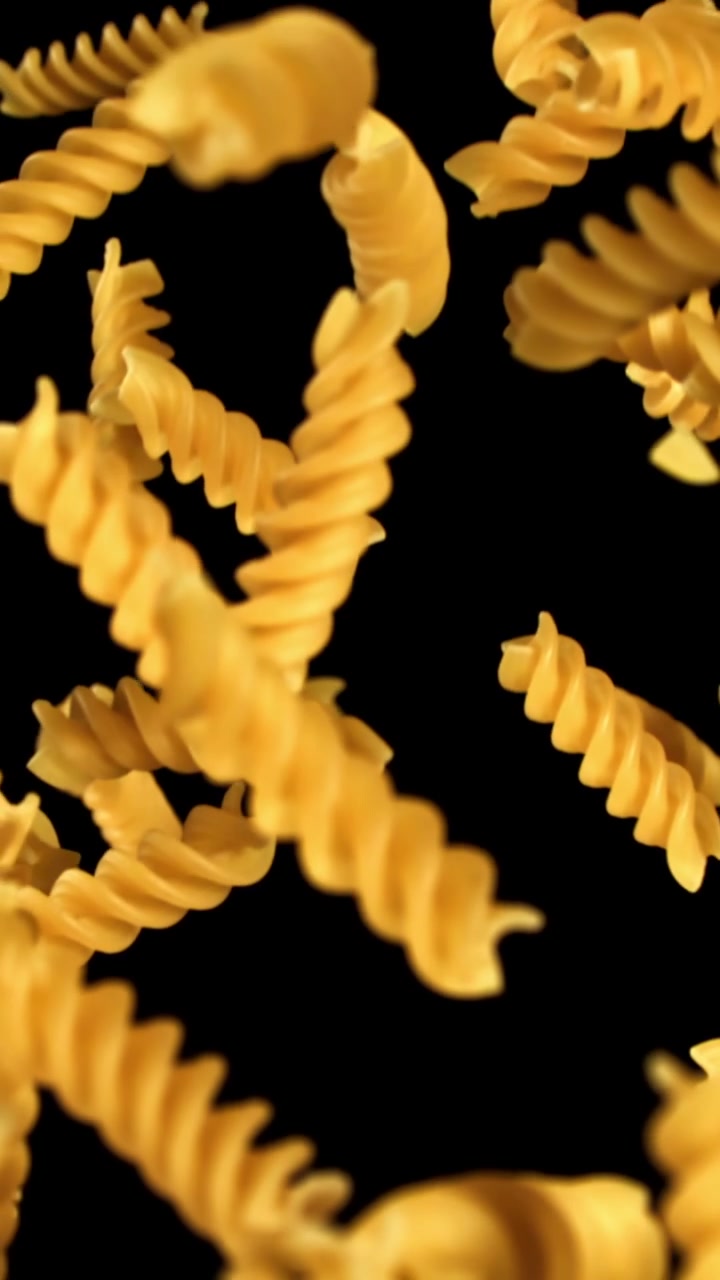 Massa fusilli dourada caindo em câmera lenta contra fundo preto