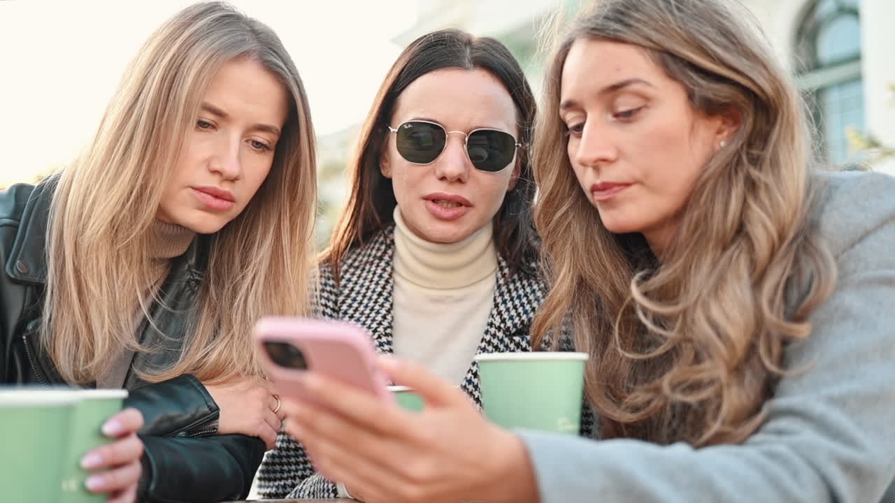 Three women going through a phone at a terrace