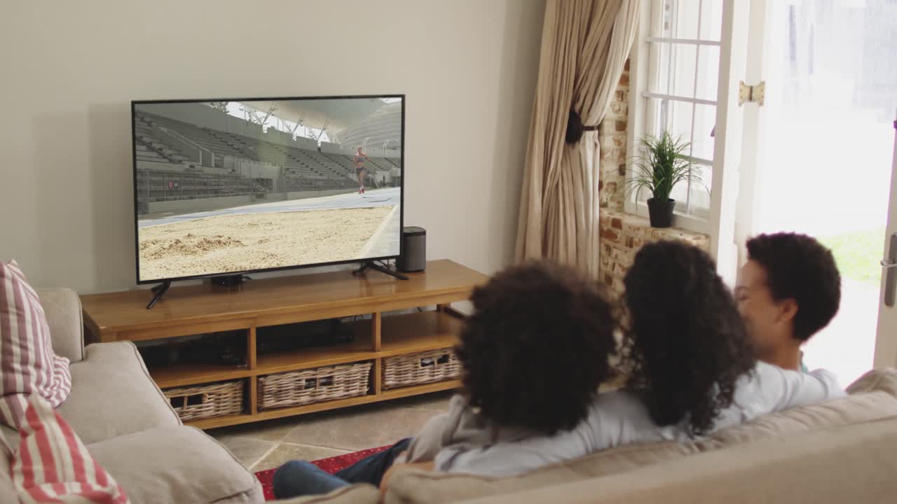 Composizione: famiglia felice seduta a casa insieme che guarda l'atletica del salto in lungo in TV.