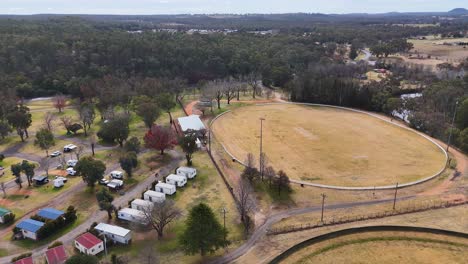 drone camera glides above a dry sports field and nearby residential area in a rural australian neighborhood, under overcast daylight with steady movement