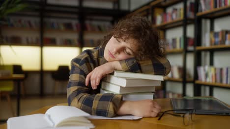 a girl with curly hair in a plaid shirt lies on a stack of books at the table and sleeps in the library