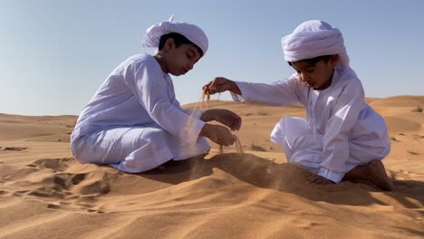 two emarati children playing with sand in the desert