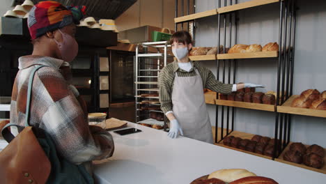 african american woman in mask buying bread in bakery