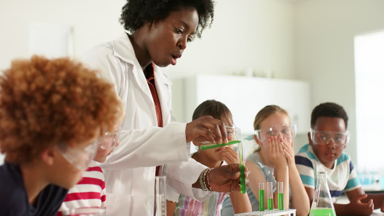 Insegnante afroamericana in camice da laboratorio e cinque adolescenti che versano liquido verde in provette, durante la lezione