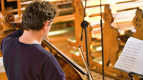 over-the-shoulder of male cellist playing in a string quartet in a small, bright church