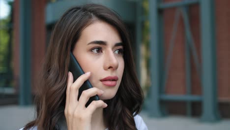 close-up view of caucasian student woman talking on the smartphone in the street and looking at camera