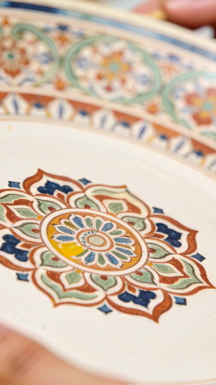 Video verticale: Una mano dipinge un tratto, riempiendo un mandala su un piatto al tavolo con un pennello che rifinisce il motivo.