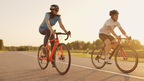 Steadicam-shot-of-two-healthy-mem-and-woman-peddling-fast-with-cycling-road-bicycle-at-sunset