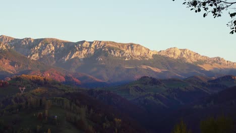 Scenery-Of-Limestone-Ridge-With-Dense-Forest-Autumn-Trees-Under-Bright-Sky-In-Piatra-Craiului,-Brasov-County,-Romania,-Panning-Left