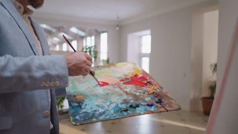 man mixes red color on palette closeup. art master in formal blue jacket prepares perfect shade in workshop. creative activity and relaxing hobby