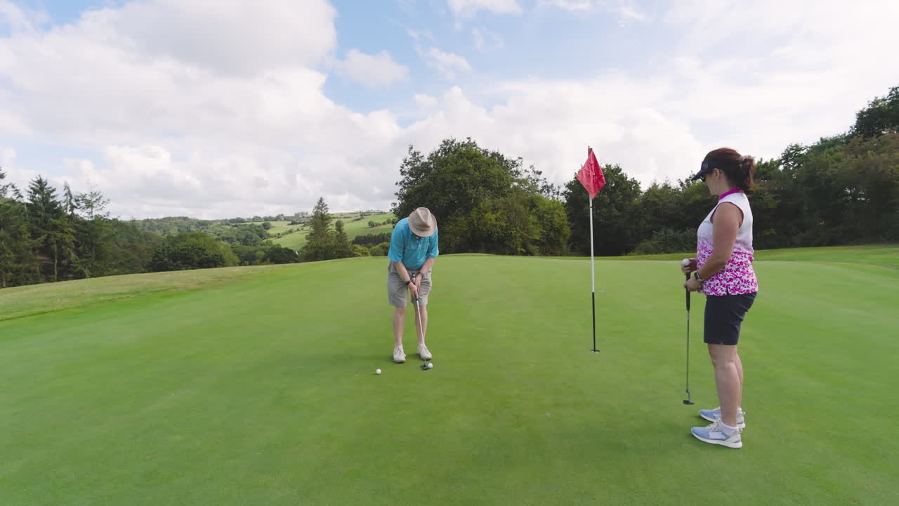 Male and female golf players playing golf and knocking golf ball into cup on golf course, copy space
