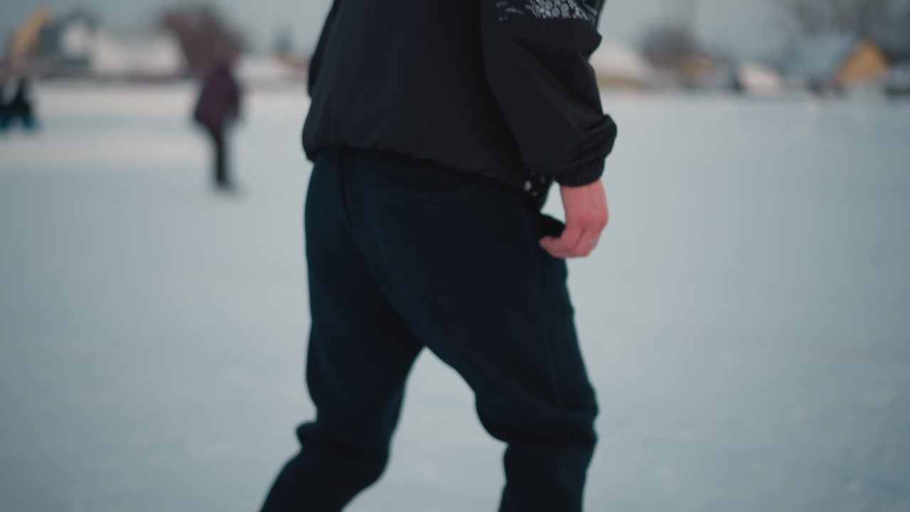 close up of person gliding on smooth frozen ice surface with blurred people in background enjoying winter outdoor activity near urban residential area under soft light dusk sky