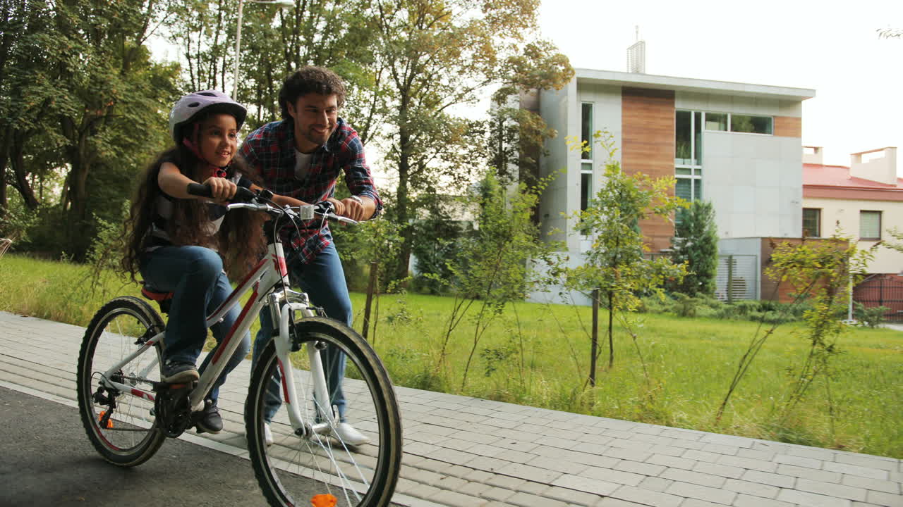 primer plano. retrato de una niña. su padre le está enseñando a andar en bicicleta. la deja ir. niña feliz mirando a la cámara. cámara en movimiento. fondo borroso