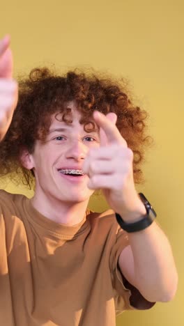 cheerful young man shows rock hand gesture with playful expression indoors a young man with a mix of african and caucasian features smiles widely sticking out his tongue while making a rock hand gesture the vibrant yellow background adds energy to the moment