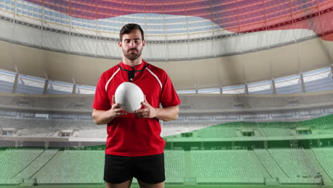 jugador de rugby profesional de pie frente a una bandera y un estadio