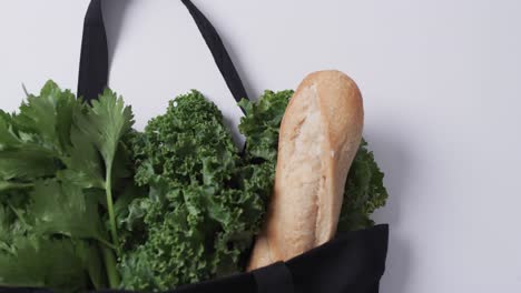 video of black canvas bag with parsley, kale and baguette, copy space on white background