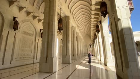 an asian female tourist wearing a black abaya walking in the corridors of sultan qaboos grand mosque in muscat, oman
