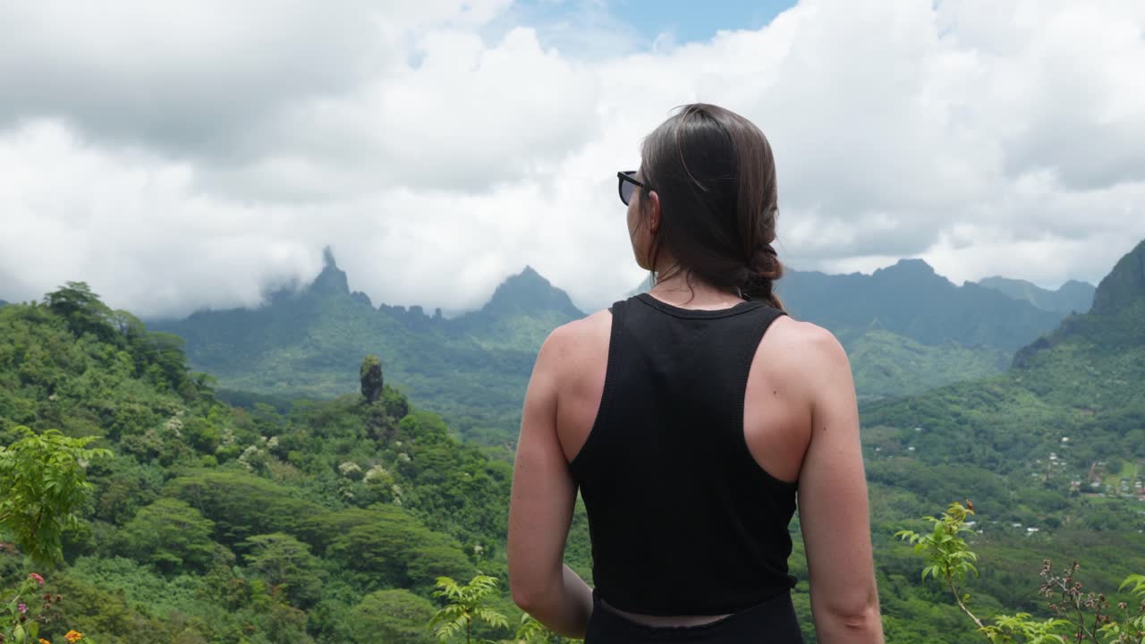 Young caucasian woman with sunglasses looking at a mountains on a sunny day in a tropical island with mountains in background in Mouaputa, Moorea, French Polynesia.