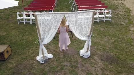 Stunning-aerial-flight-slowly-sinking-down-drone-shot-from-behind-of-a-free-wedding-speaker-speaks-in-front-of-empty-seats-in-nature-by-the-lake-a-summer