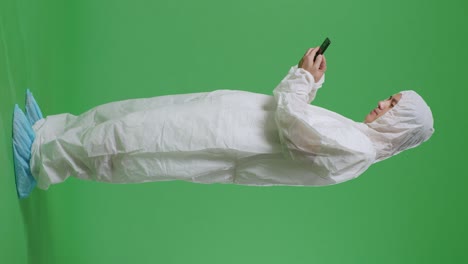 녹색 화면 배경에 서서 스마트폰을 사용하는 아시아 남성 과학자의 전체 몸 측면 시각