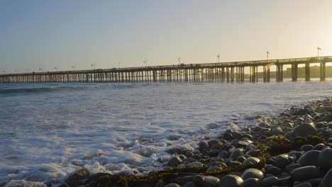 panning shot of the ventura pier with sunsetting in the background while waves are crashing along the shores of ventura beach located in southern california