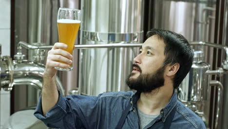 Professional-Brewery-Worker-Examining-Glass-Of-Freshly-Brewed-Unfiltered-Beer,-Drinking-It-And-Looking-At-Camera-While-Checking-Beverage-Quality-At-Plant