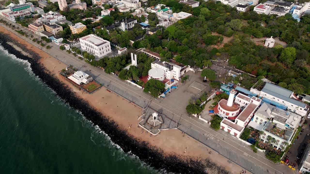 This early morning aerial video captures Puducherry's coastline from the water. The footage highlights the iconic Mahatma Gandhi statue and a lighthouse, with waves from the sea rolling onto the shore