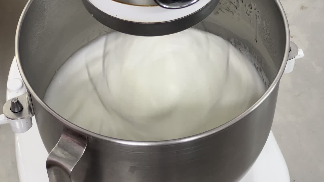 configuración de panadería comercial toma de primer plano de batidora eléctrica mezclando clara de huevo y azúcar hasta que sea un pico brillante y un pico rígido, preparando crema de mantequilla de merengue