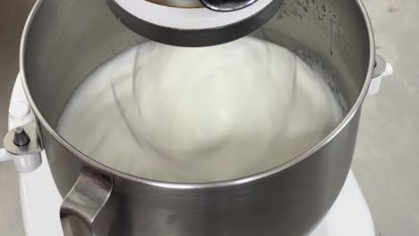 commercial bakery setting close up shot of electric mixer mixing egg white and sugar until it is glossy peak and stiff peak, preparing meringue buttercream