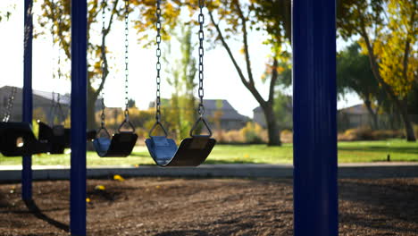 Slide left through a kids playground in a park at sunrise with an empty swing set