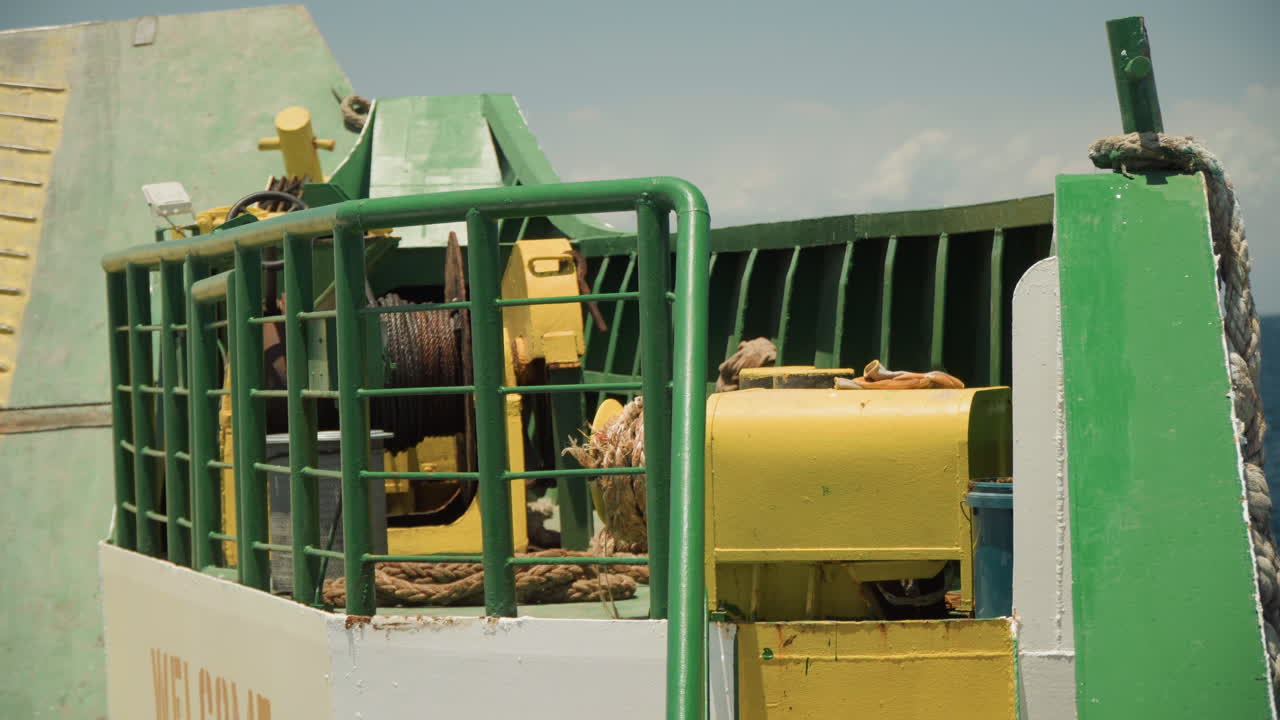 Manutenzione dell'operatore dell'argano a gabbia di una macchina verde, primo piano di tamburo metallico, cavo, ingranaggi e componenti idraulici su attrezzature da costruzione usurate, operaio con casco ispeziona la protezione, luce solare intensa.